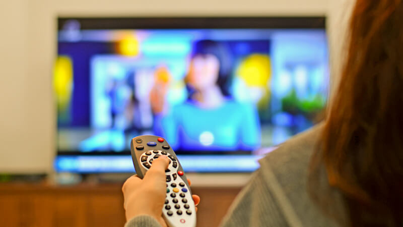 Woman holding a remote control for a smart TV.  The smart TV featuring a targeted OTT ad is in the background.