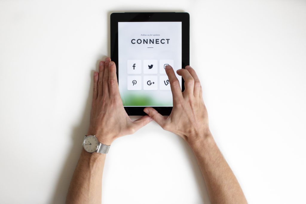A pair of hands using a tablet to connect with a brand through various social media platforms