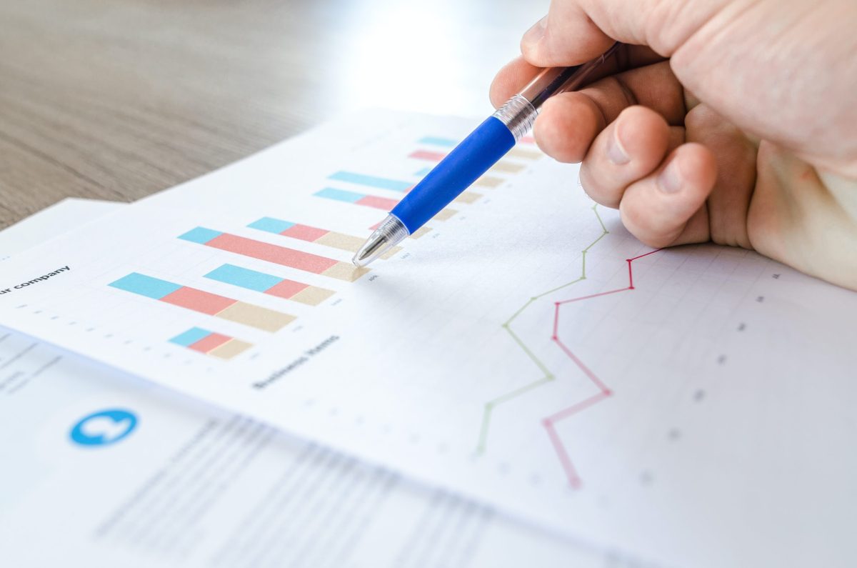 A hand holding a pen that is pointed at a graph that shows key business metrics