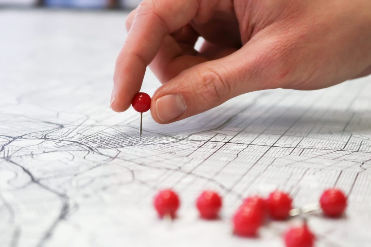 A hand placing a pin onto a location that is shown on a map.