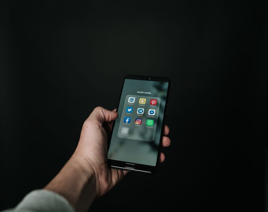 A hand holding an Iphone with the screen displaying various apps