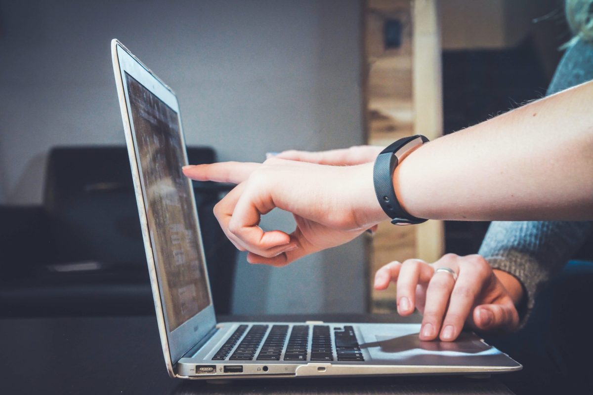 Two people looking at a laptop while a hand is pointing at the screen