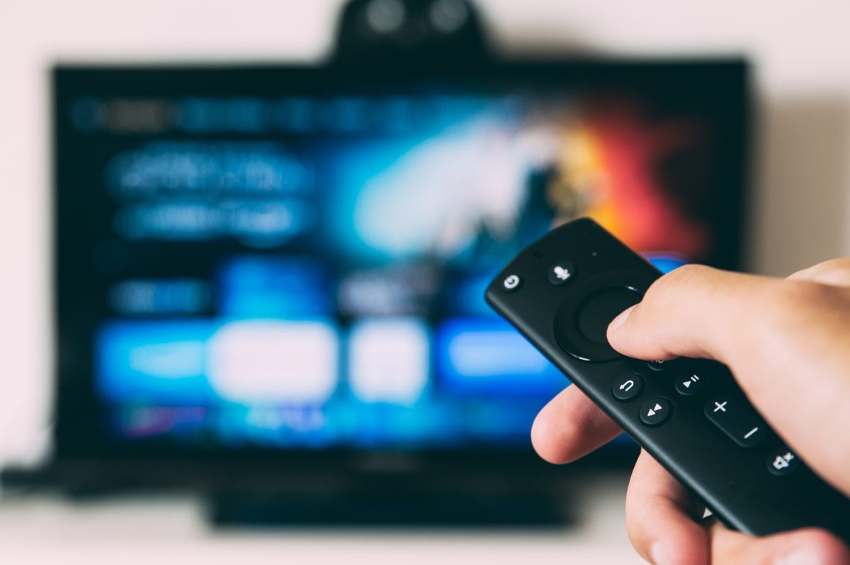 A hand holding a remote that is pointing to a smart tv