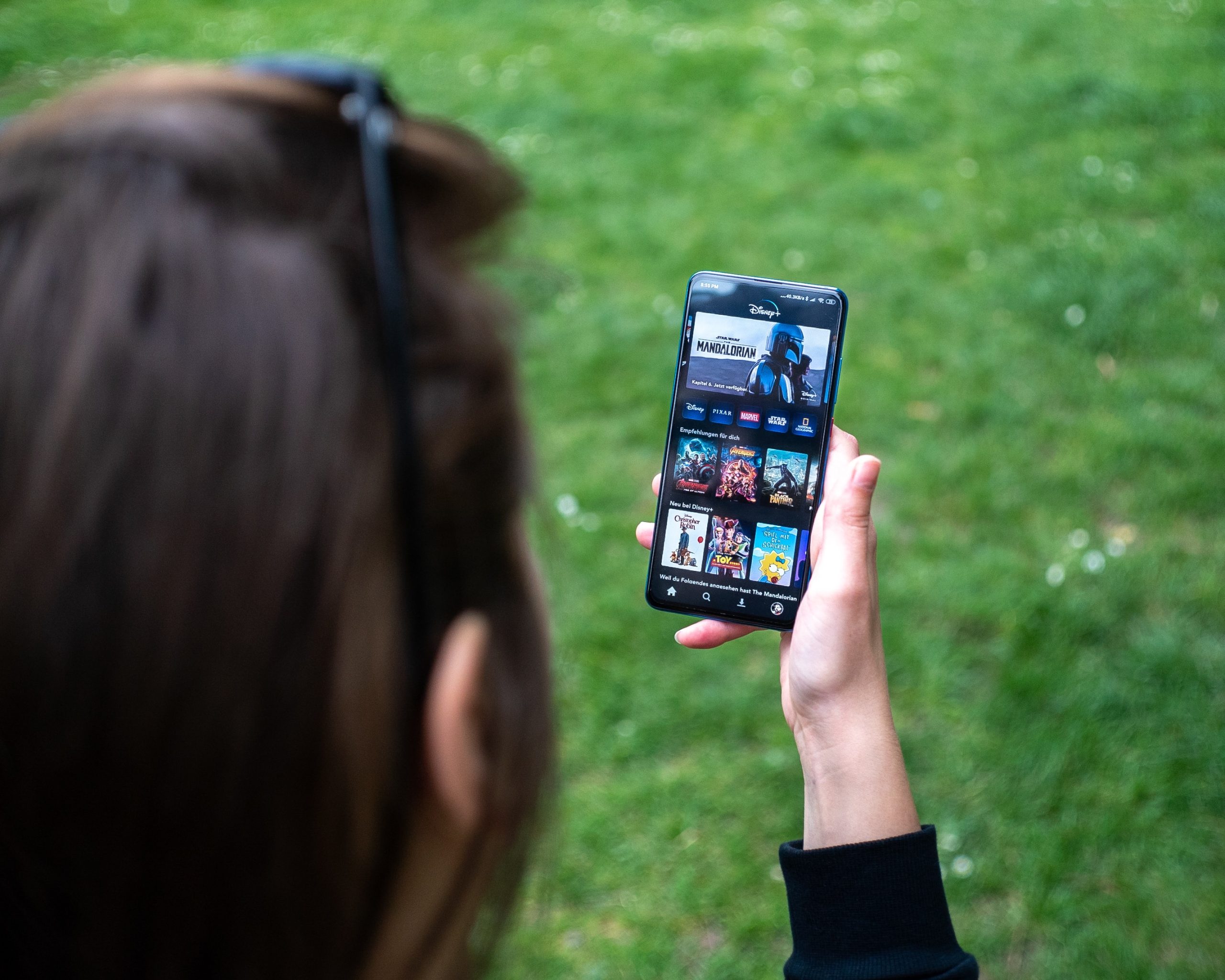 A woman holding a mobile phone while the screen displays Disney+ homepage