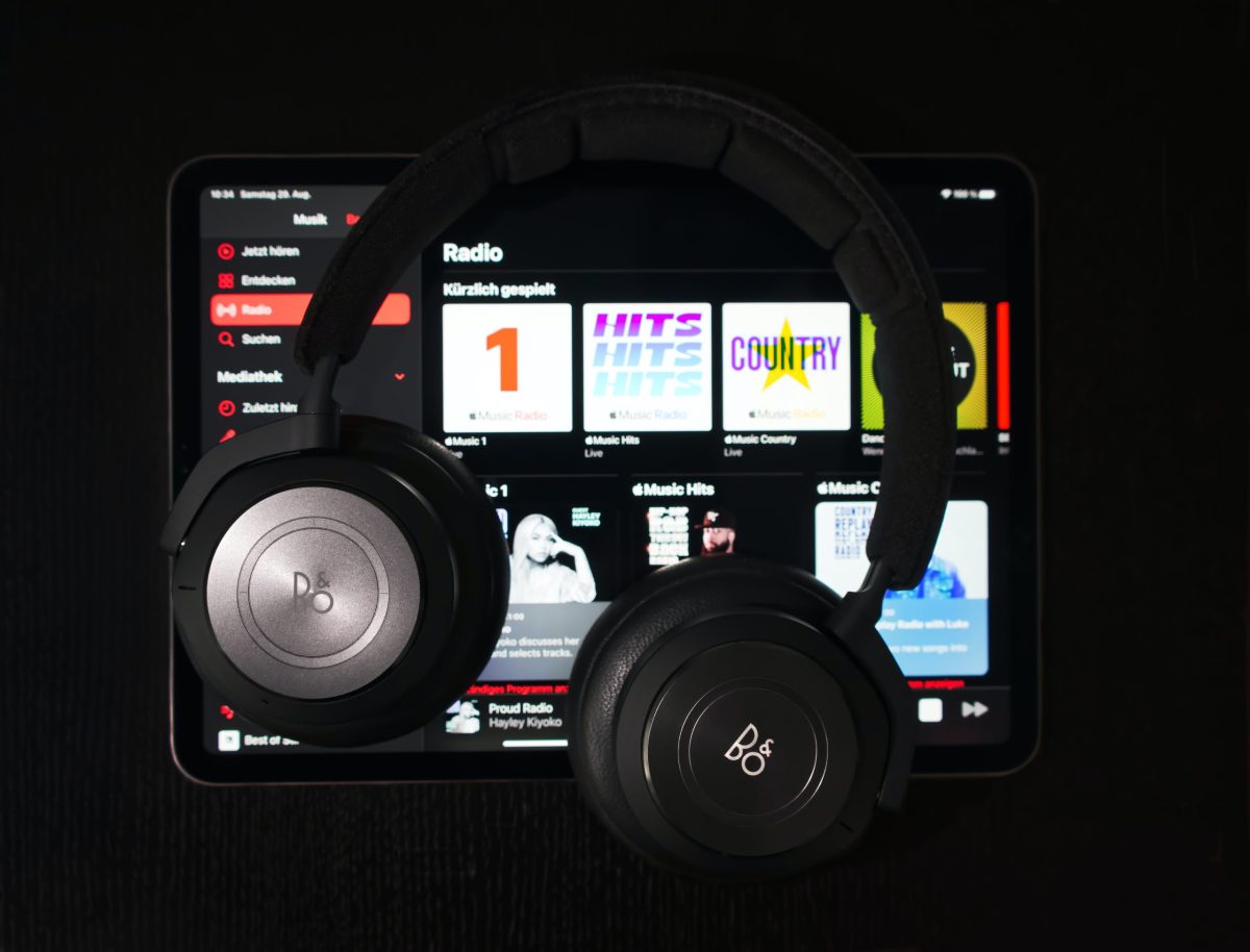 A tablet with a pair of headphones laying on top of it. The screen shows a music streaming service