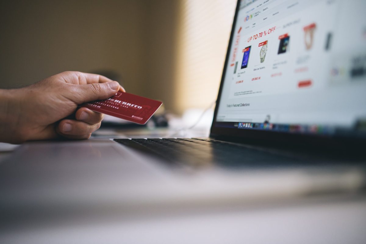 A hand holding a credit card while shopping on a laptop