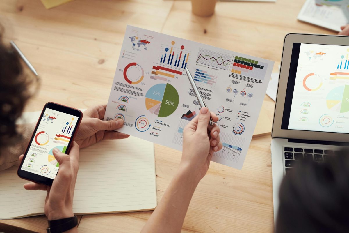 A hand pointing to a paper that is displaying multiple charts and graphs