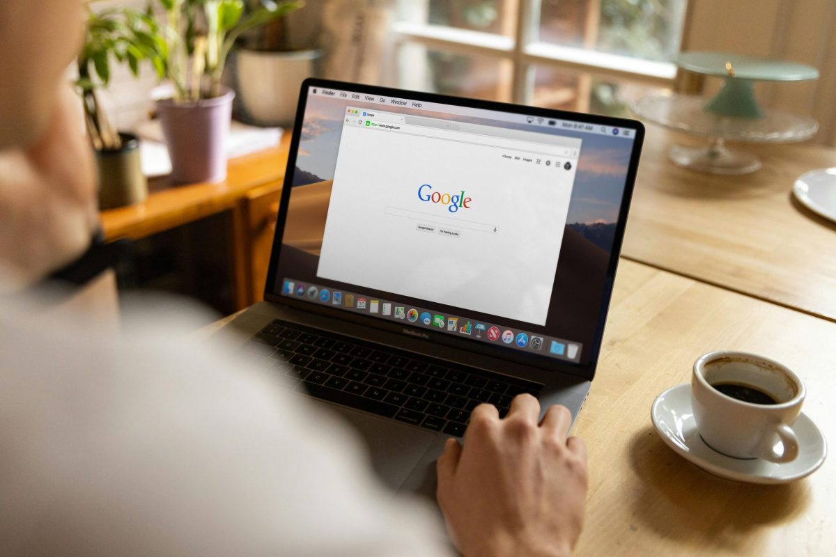 jakob-owens-WUmb_eBrpjs-unsplash Person using a MacBook Pro with Google open on the screen, sitting at a wooden table with a cup of black coffee