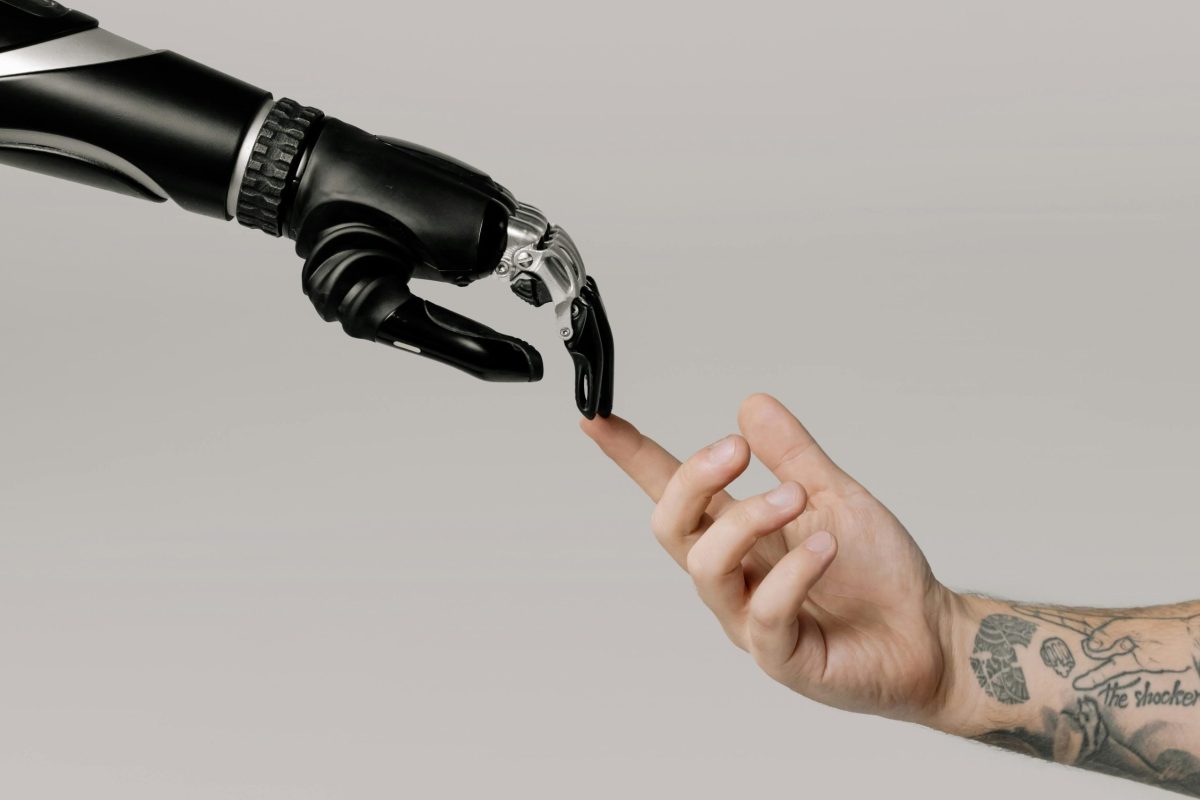 jakob-owens-WUmb_eBrpjs-unsplash A close-up of a robotic hand and a human hand reaching towards each other, with their fingertips touching